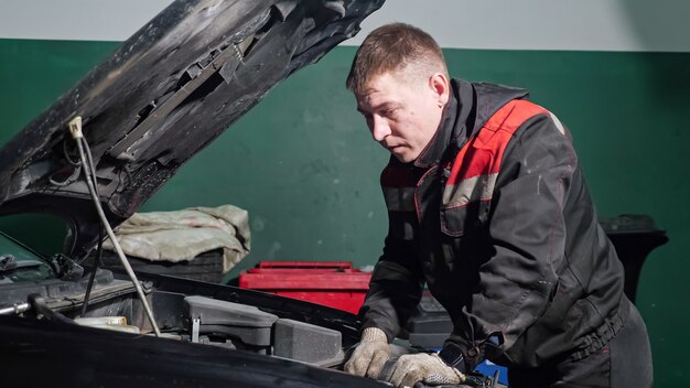 young-worker-uniform-examines-fix-broken-automobile